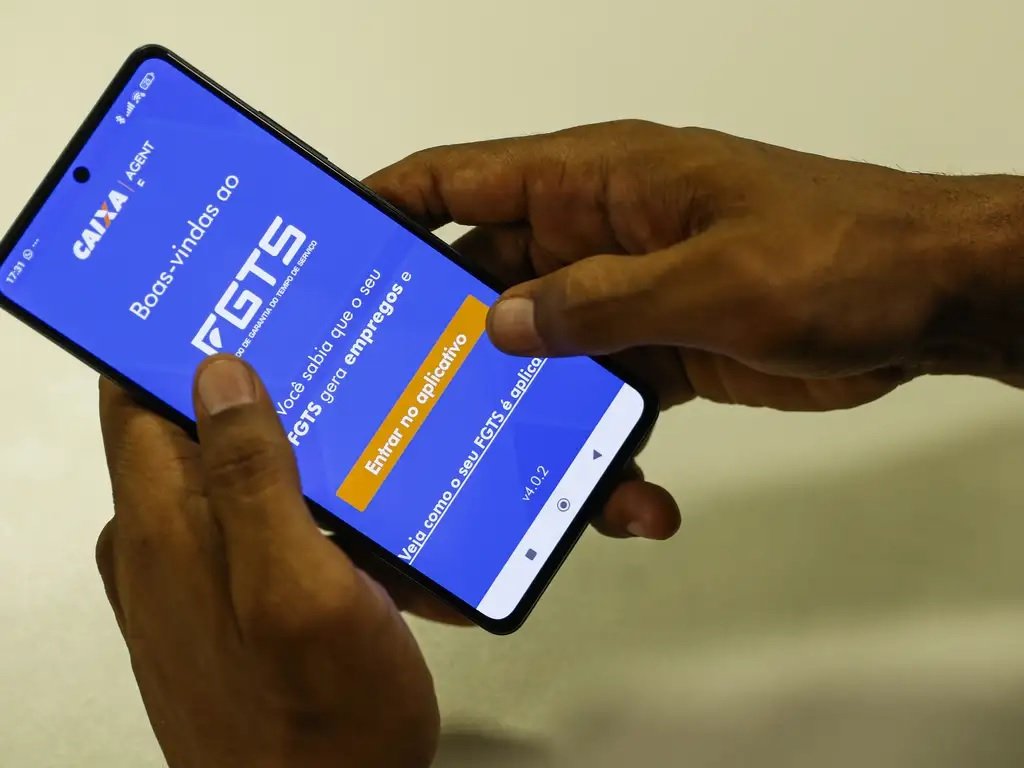 Mãos de homem negro olhando, mexendo em aplicativo do fgts