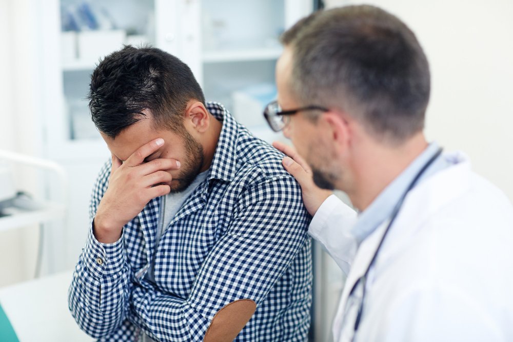 Homem sentado sendo consolado por médico