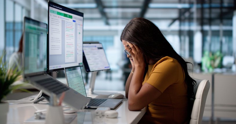 Mulher diante de computador cobrindo o rosto com as mãos