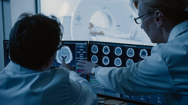 Médicas examinam imagens enquanto paciente se submete a exame de ressonância magnética