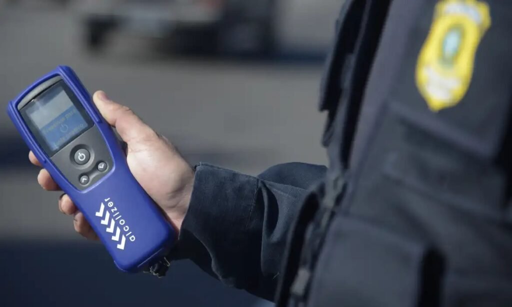 Policial todoviário segurando equipamento de teste do bafômetro