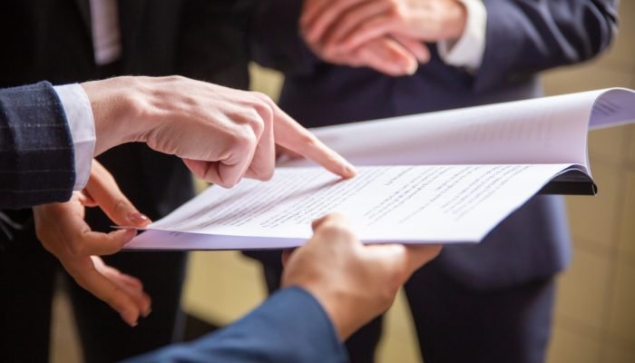 Grupo de pessoas em pé e com roupa social analisam contrato