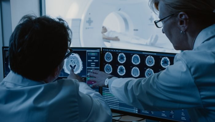 Médicas examinam imagens enquanto paciente se submete a exame de ressonância magnética