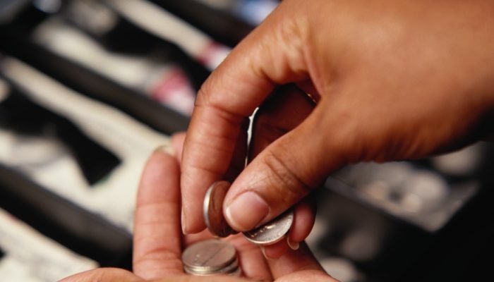 Detalhe de mão contando moedas numa caixa registradora