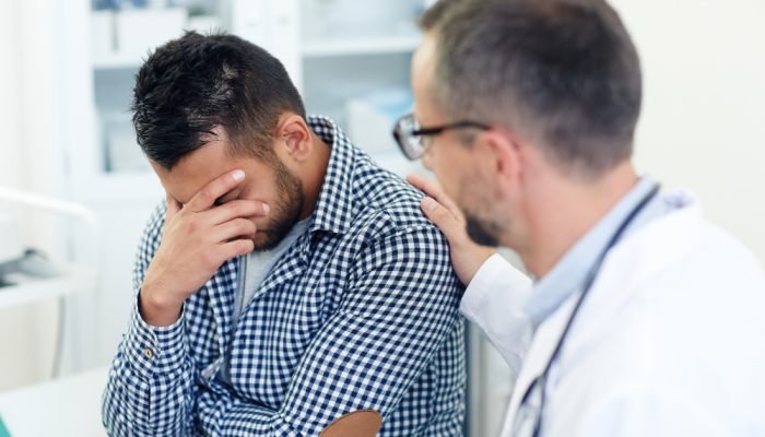 Homem sentado sendo consolado por médico