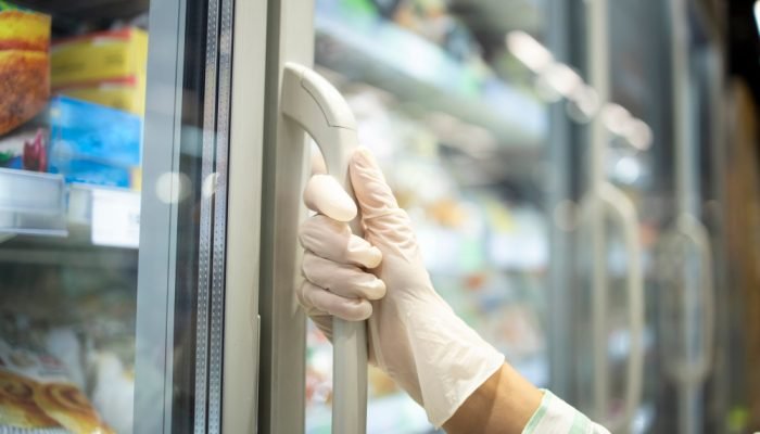 Mão de mulher com luva abrindo frezeer de produtos em câmera fria
