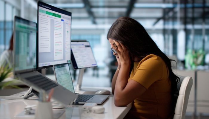 Mulher diante de computador cobrindo o rosto com as mãos
